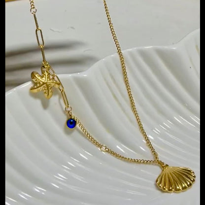 Gold necklace with starfish and shell pendant on a white surface